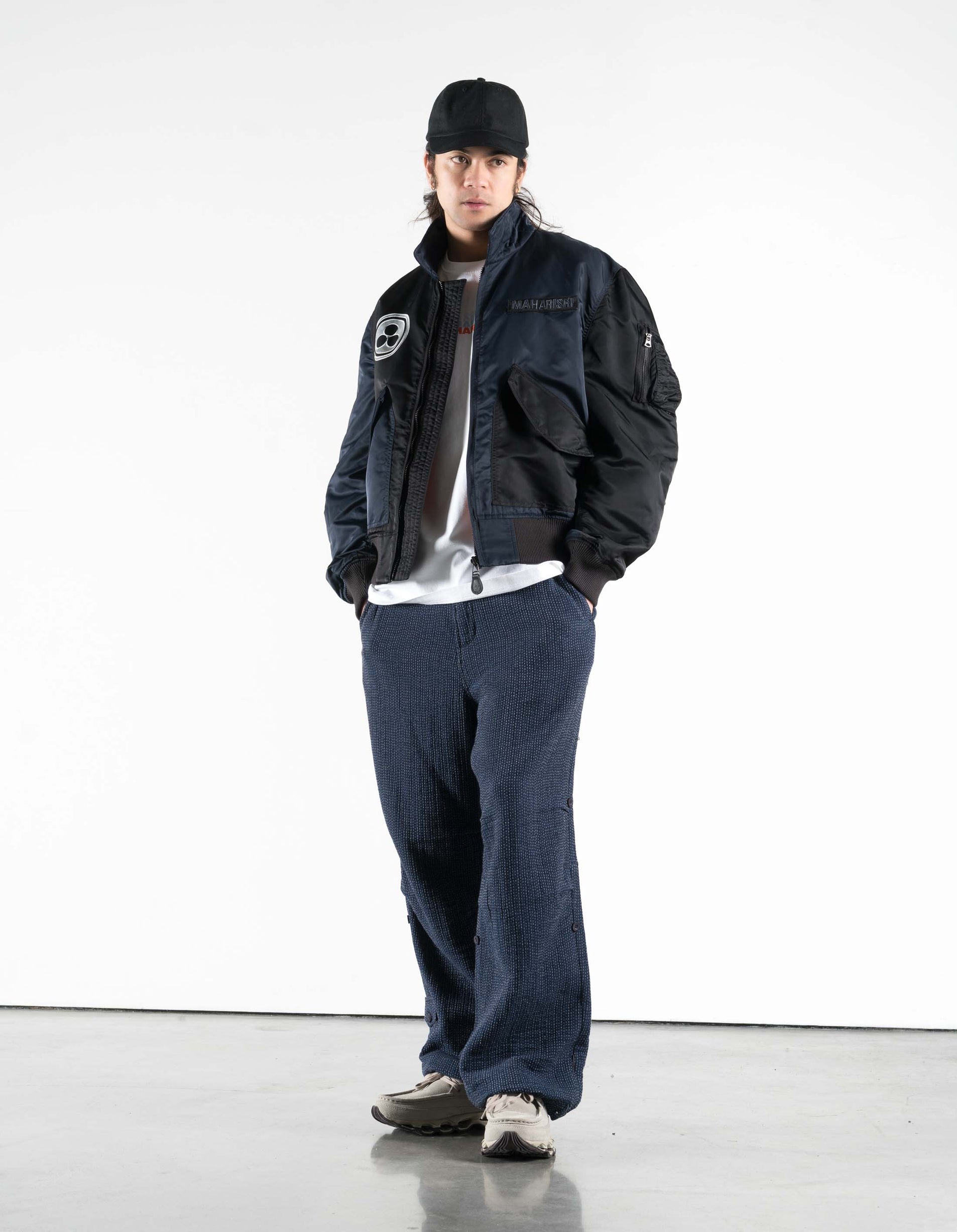 Person wearing a dark jacket, cap, and jeans on a white background