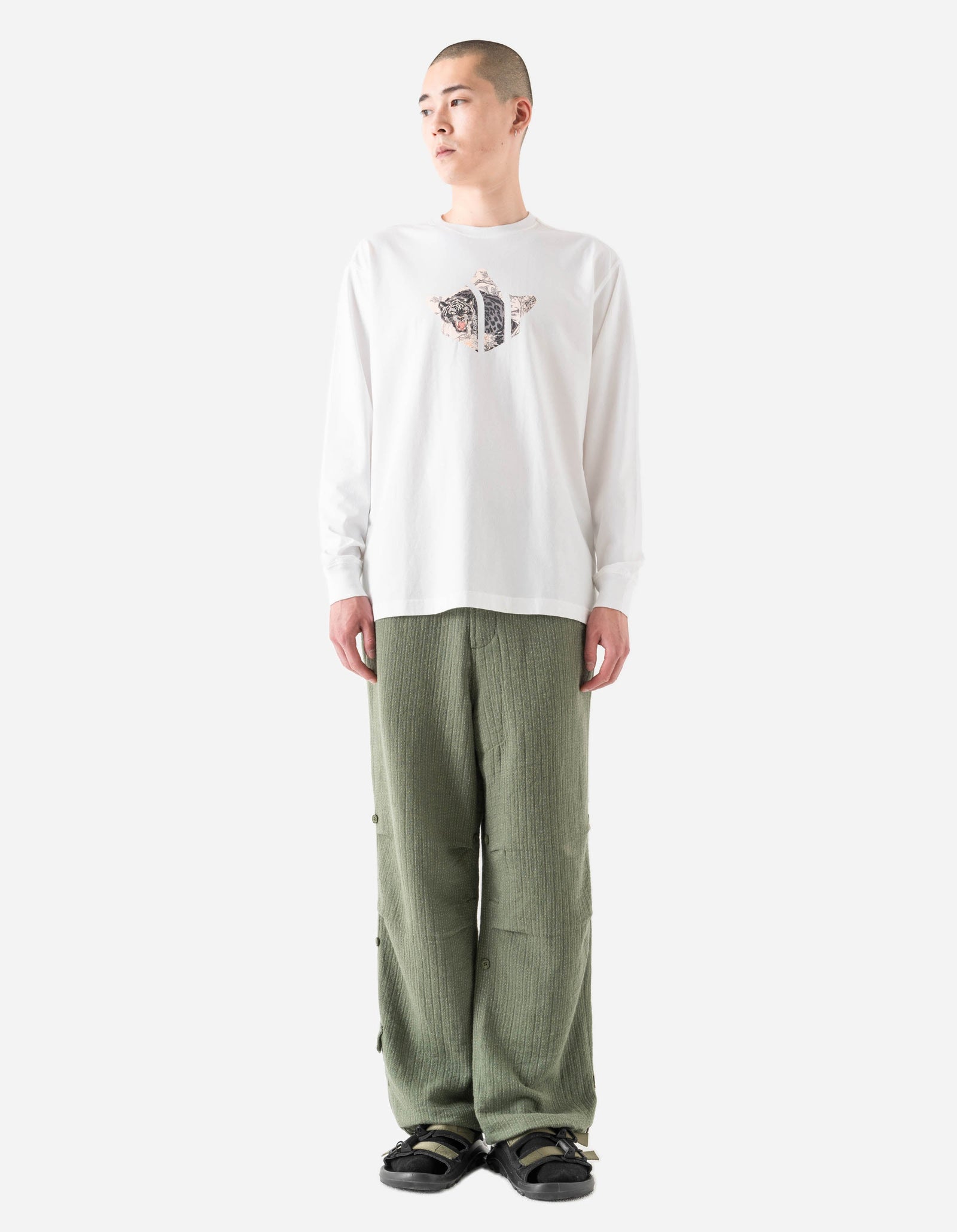 Person wearing a white long-sleeve shirt with a graphic design and green pants on a white background