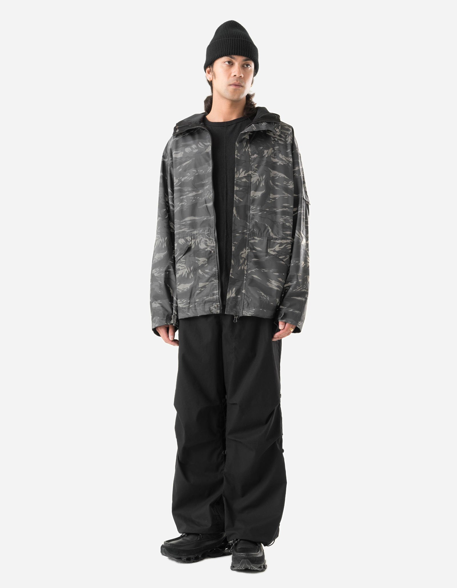 Person wearing a camouflage jacket and black pants on a white background