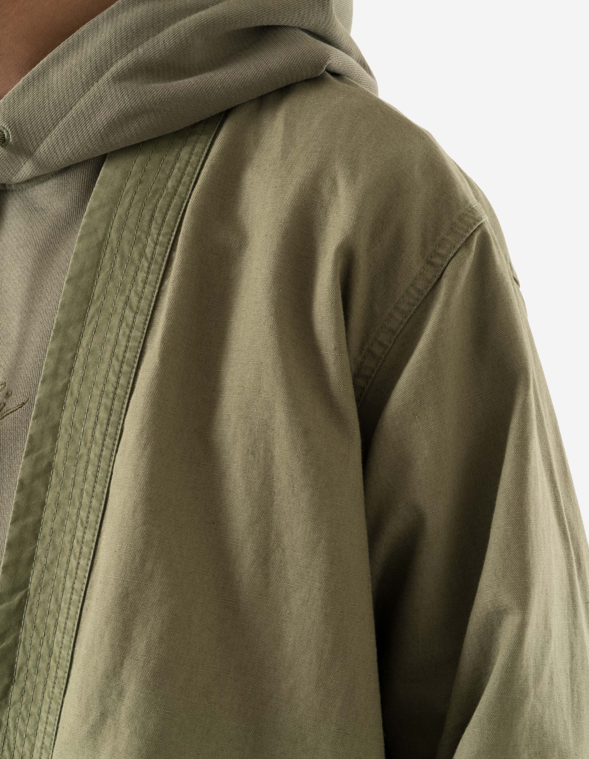 Close-up of a person wearing a green jacket with a hood on a light gray background