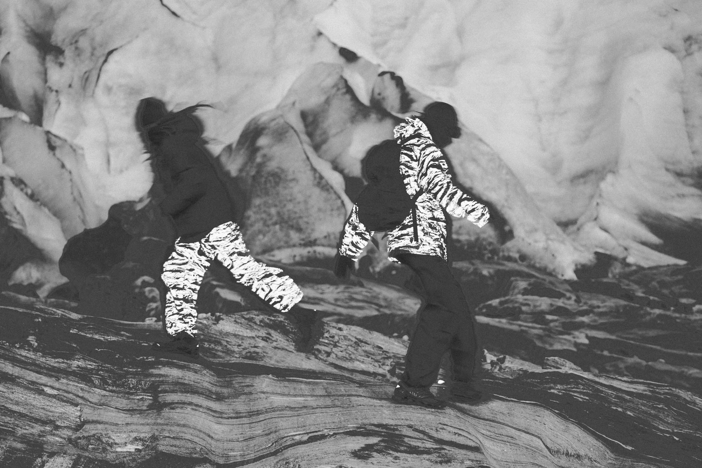 Two people in zebra-patterned jackets standing on a rocky surface with ice formations in the background.