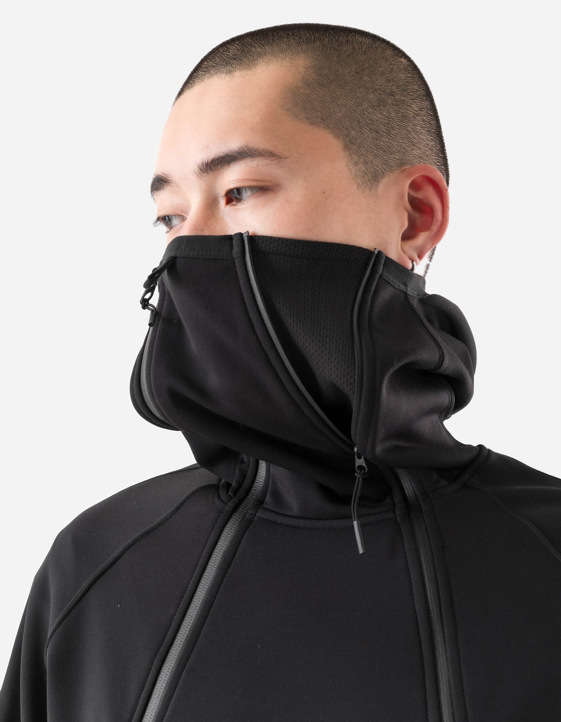 Person wearing a black hooded garment with a zipper on a white background