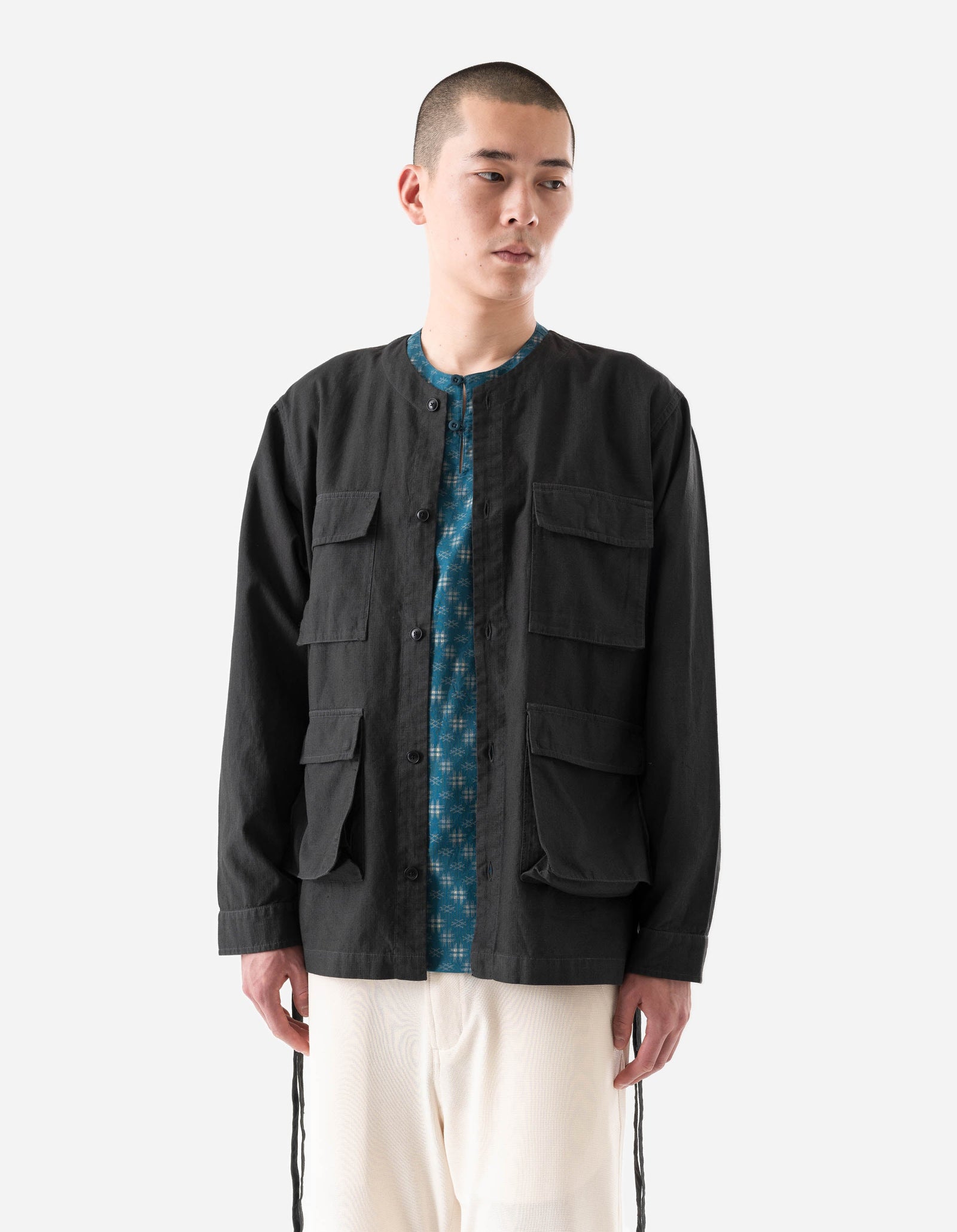 Man wearing a black jacket over a patterned shirt on a white background