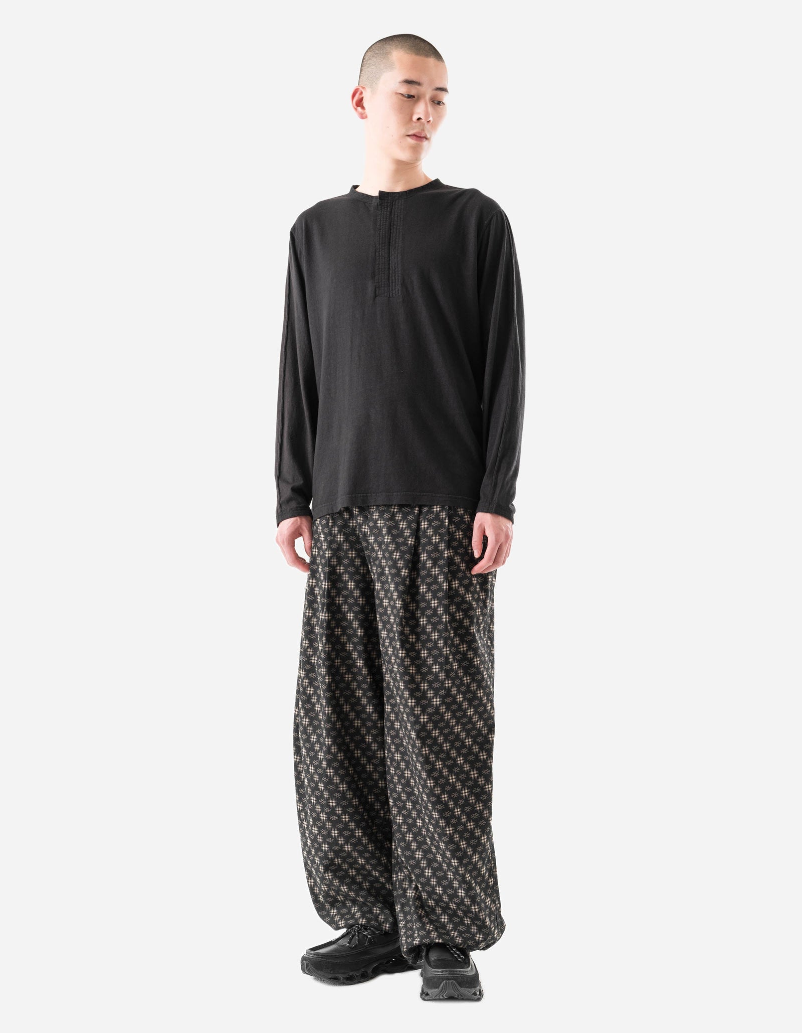 Person wearing a black long-sleeve shirt and patterned pants on a white background